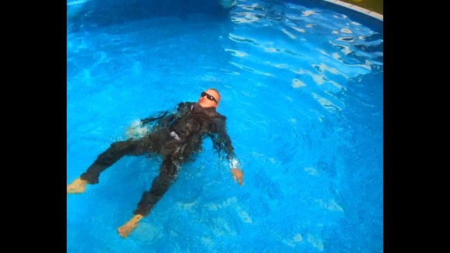 Video Reference: swimming pool, person, floating, back float, blue water, sunglasses, dark clothing, recreation, leisure, outdoors, water, relaxation