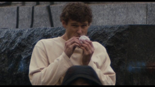 Video Reference: person, young adult, sweater, holding object, outdoor, stone wall, fountain, close-up, portrait, crowd, winter, blurred background