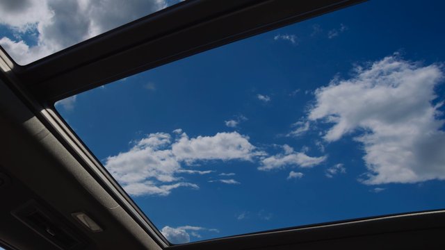 Video Reference: sky, clouds, sunroof, car interior, vehicle, blue sky, travel, daytime, window, open roof, outdoors, view from inside