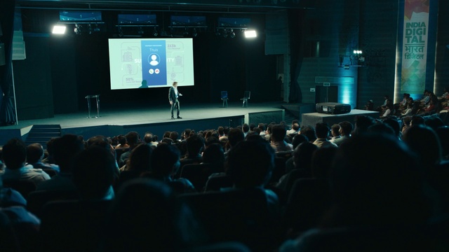 Video Reference: Entertainment, Projection screen, Crowd, Event, Display device, Stage equipment, Chair, Audience, Projector accessory, Public speaking