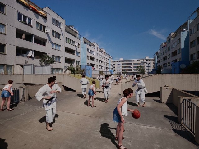 Video Reference: courtyard, apartment buildings, martial arts, karate, children, outdoor, urban, summer, basketball, residential, group, practice, playground, architecture, daylight