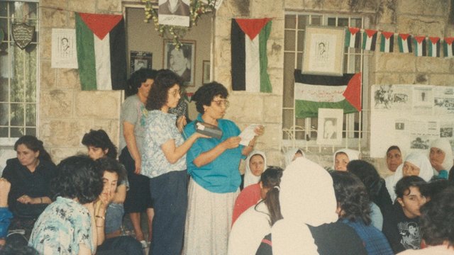 Video Reference: indoor, group, women, meeting, reading, papers, flags, posters, stone wall, community, gathering, crowd, cultural event, historical photo, portrait, seated