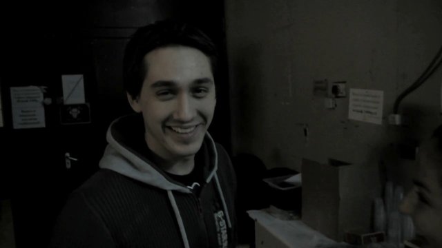 Video Reference: man, smiling, hoodie, indoors, portrait, dim light, casual, young adult, room, background clutter, standing, close-up