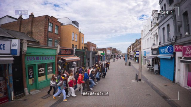 Video Reference: street, pedestrians, crossing, shopping street, storefronts, city, urban, buildings, group, daytime, cloudy sky, cctv, recording, high street, walkway, crowd