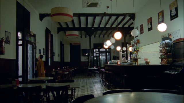 Video Reference: cafe, interior, empty tables, hanging lights, counter, vintage decor, restaurant, indoor, tiles, person, doorway, dim lighting, cozy, coffee shop, wide shot