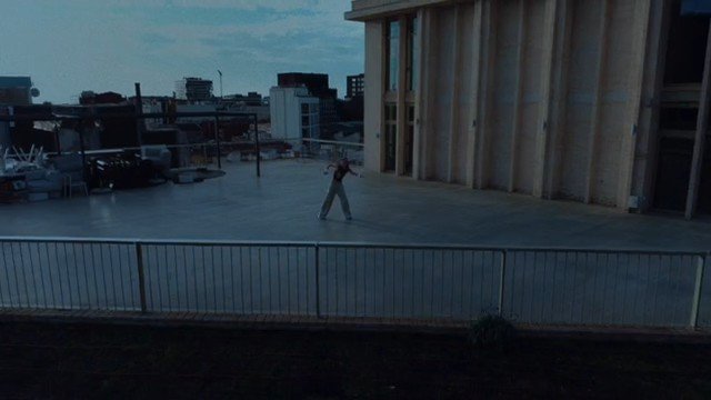 Video Reference: rooftop, terrace, cityscape, dusk, person, outdoors, urban, building, wide shot, concrete, railing, empty space