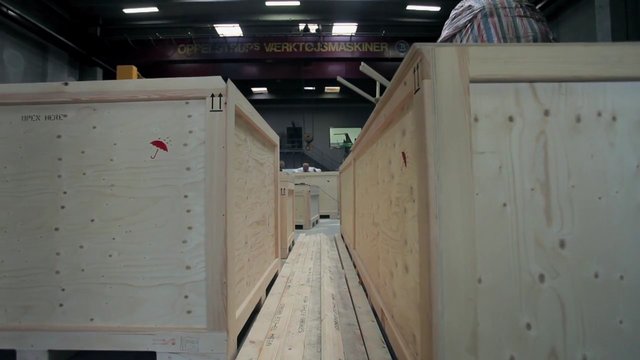 Video Reference: warehouse, wooden crates, shipping boxes, loading area, industrial, storage, pallets, aisle, indoor, packing, freight, cargo, wood, fluorescent lights
