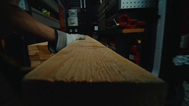 Video Reference: wood, plank, construction, carrying, glove, storage, narrow aisle, interior, workshop, materials, manual labor, close-up