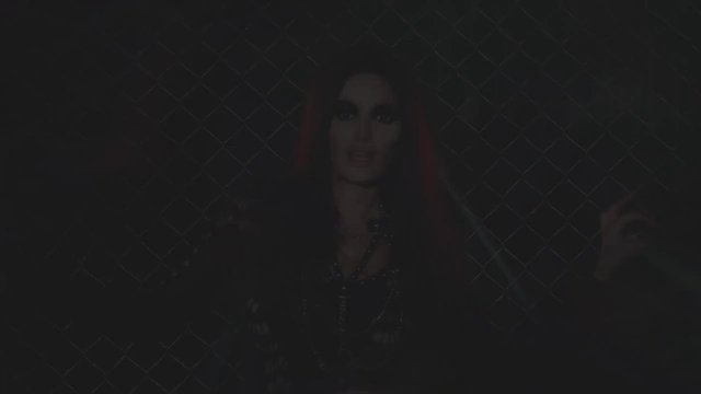 Video Reference: dark, person, standing, chain-link fence, portrait, low light, outdoor, fence, long hair, dark clothing
