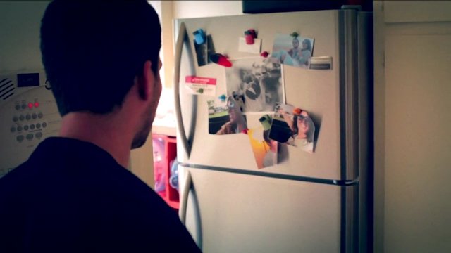 Video Reference: kitchen, refrigerator, person, indoor, home, photos, magnets, appliance, back view, family pictures