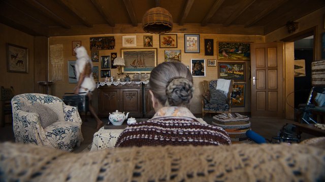 Video Reference: living room, interior, vintage decor, paintings, crochet, furniture, home, person, back view, wood paneling, warm light, ornate, cabinet, chair, table, domestic