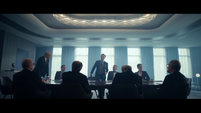 Video Reference: Outerwear, Coat, Table, Interaction, Suit, Public speaking, Electronic device, Presentation, Projection screen, Event