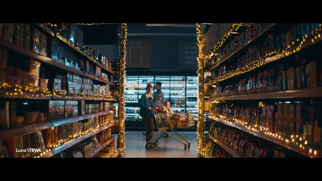 Video Reference: supermarket, grocery store, aisle, shopping cart, family, child, shelves, packaged goods, string lights, indoor, retail, nighttime, store interior
