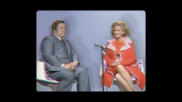 Video Reference: Outerwear, Microphone, Leg, Coat, Smile, Dress, Gesture, Television program, Thigh, Tie