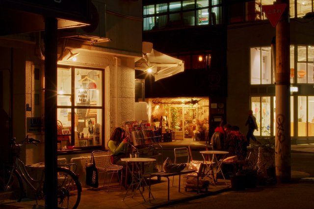 Video Reference: night, street, coffee shop, cafe, outdoor seating, storefront, urban, warm lights, bicycle, pedestrian, window display, sidewalk, city, evening, interior glow, quiet