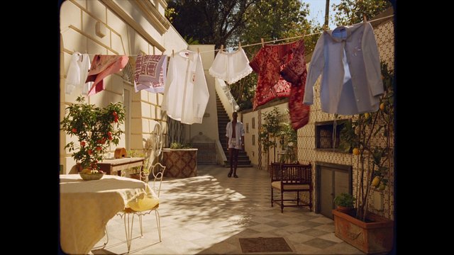 Video Reference: courtyard, laundry, clothesline, sunlight, outdoor, building, potted plants, tiles, residential, patio, garden, street scene, shirt, linen, shadows, person