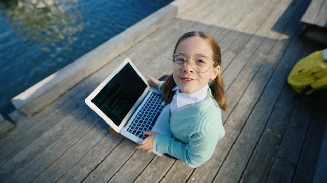 Video Reference: girl, child, glasses, laptop, dock, wooden deck, water, outdoor, technology, smiling, overhead view, summer, education, programming