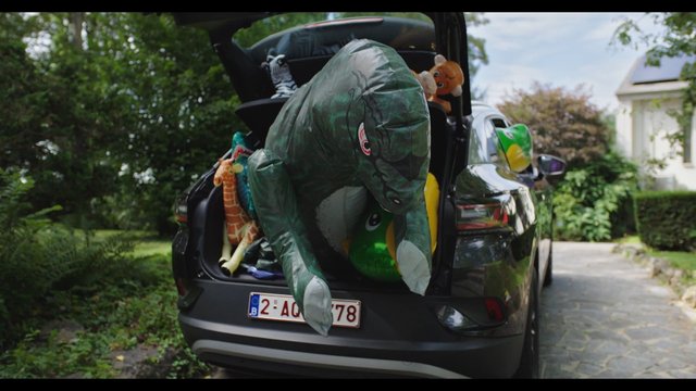 Video Reference: SUV, car trunk, open hatch, inflatable toys, stuffed animals, driveway, outdoors, residential area, trees, house, parked vehicle, colorful, playful, summer