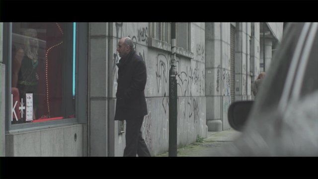 Video Reference: street, urban, sidewalk, man, coat, storefront, window, graffiti, city, pedestrian, car, outdoor, building, side view, daytime