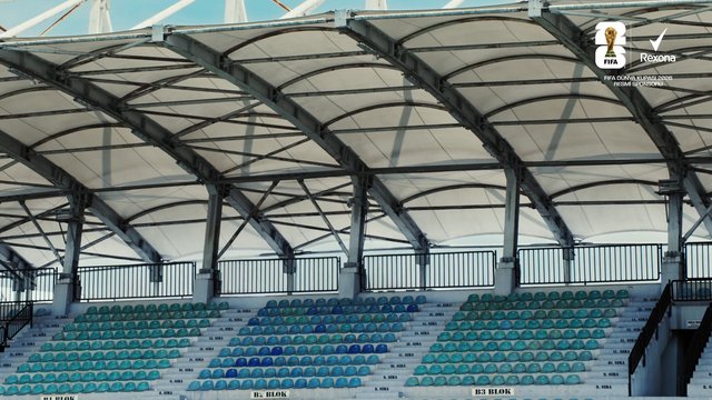 Video Reference: stadium, sports venue, seating, empty stands, roof structure, arena, architecture, indoor-outdoor, bleachers, football, soccer, canopy, sponsorship, text overlay