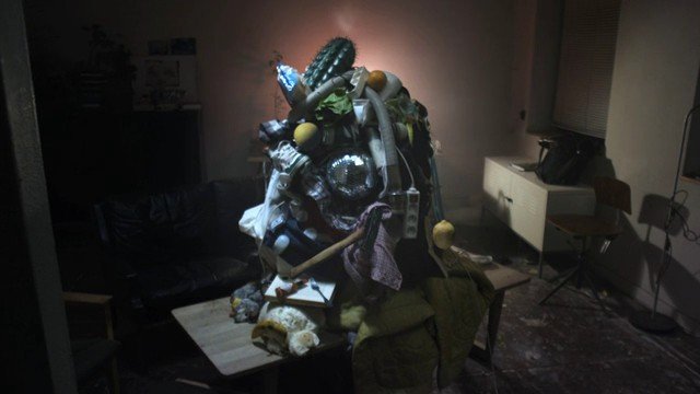 Video Reference: dim interior, clutter, junk pile, mixed objects, table, couch, cabinet, window blinds, shadows, messy room, indoor, pile of debris