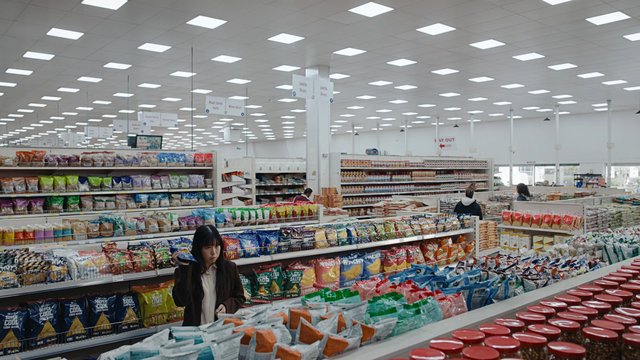 Video Reference: supermarket, grocery store, aisle, shelves, packaged food, snacks, dry goods, shopping, interior, bright lights, retail, shoppers, food market, aisle signs, store