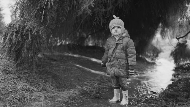 Video Reference: child, winter, outdoors, black and white, tree, forest, muddy path, water, coat, hat, boots, standing, nature, portrait, cold, dusk