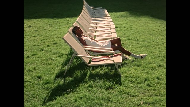 Video Reference: person, lawn, grass, outdoor, lounge chairs, reclining, summer, sunlight, white dress, tennis racket, relaxation, park, shadow, fashion, minimal, scene