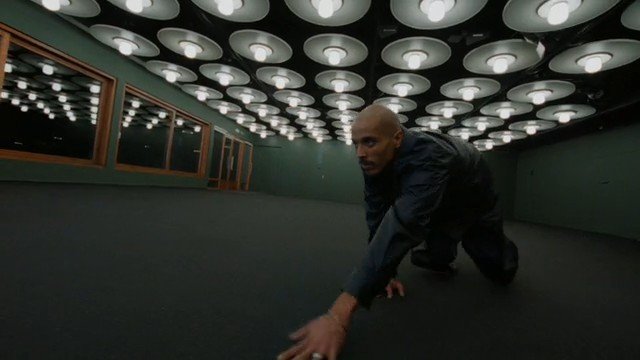 Video Reference: man, crawling, indoor, dim light, ceiling lights, room, motion, dark clothing, bald, floor level, interior, windows, dramatic, wide angle
