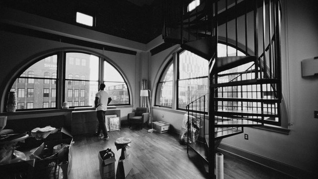 Video Reference: loft, apartment, interior, spiral staircase, arched windows, city view, black and white, person, living room, furniture, moving boxes, modern, large windows, urban, home, open space