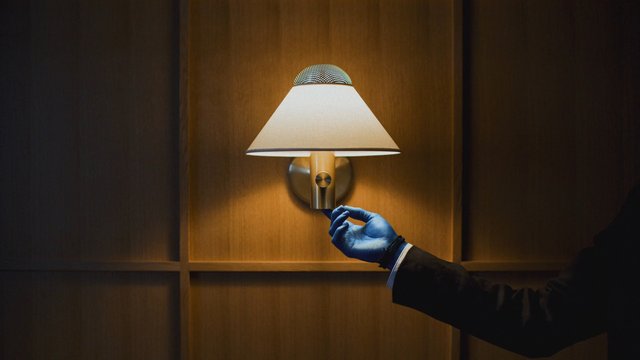 Video Reference: wall lamp, lighting, gloved hand, interior, wood panel, adjusting, sconce, hotel, office, warm light, close-up, hands, decor, modern, dimly lit