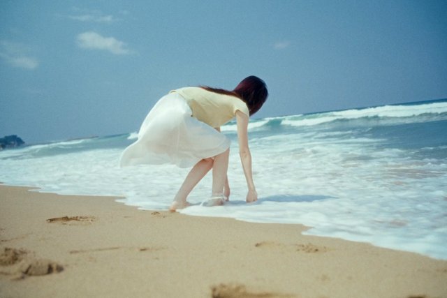 Video Reference: beach, shoreline, waves, ocean, sand, woman, dress, crouching, seaside, summer, outdoors, blue sky, coast, travel, nature