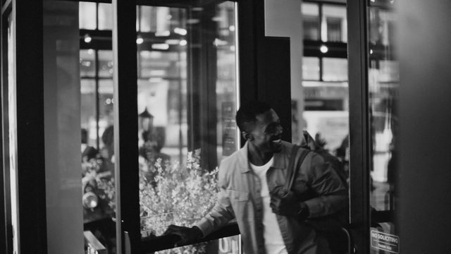 Video Reference: black and white, man, doorway, glass door, storefront, urban, entrance, reflection, indoor, outdoor, candid, street scene, building, smiling, portrait