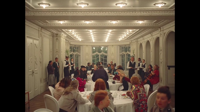 Video Reference: Furniture, Chair, Table, Lighting, Coat, Social group, Suit, Hall, Decoration, Crowd