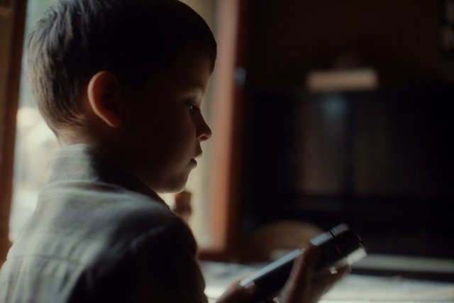 Video Reference: child, boy, profile, indoor, smartphone, window light, soft focus, low light, portrait, home, side view, candid, close-up, shallow depth of field