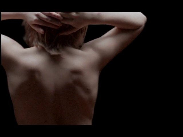 Video Reference: person, back view, bare back, arms raised, dark background, portrait, standing, upper body, silhouette, minimal scene