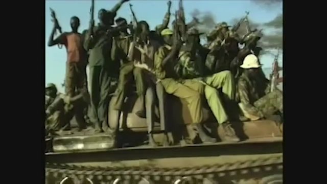 Video Reference: armed men, group, vehicle, outdoors, dry landscape, rifles, standing, sitting, military, conflict, transport, crowd, warlike, rural, daylight
