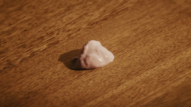 Video Reference: wooden table, small object, white blob, close-up, warm light, indoor, texture, macro, still life, food spill, surface