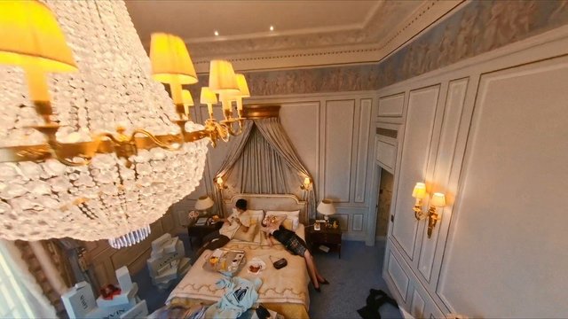 Video Reference: bedroom, hotel room, luxury interior, chandelier, bed, people, indoor, decorative wall, nightstand, lamp, clothes, messy room, relaxing, interior design, travel, room service