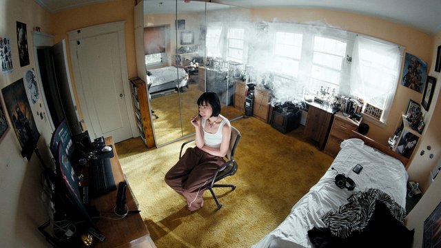 Video Reference: bedroom, person, smoking, chair, indoor, computer desk, bed, mirror, window, home interior, messy room, wide angle, daylight, casual, lifestyle