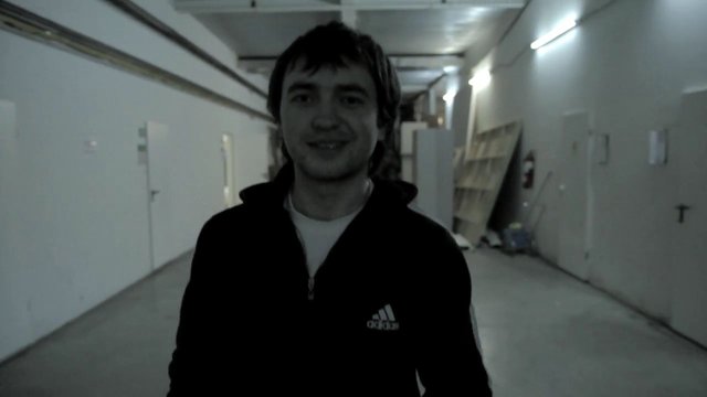 Video Reference: man, person, indoors, corridor, hallway, warehouse, standing, portrait, low_light, casual_clothing, front_view, industrial, interior