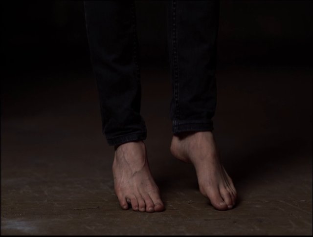 Video Reference: bare feet, feet, lower legs, jeans, standing, close-up, indoor, dim light, floor, human, casual clothing