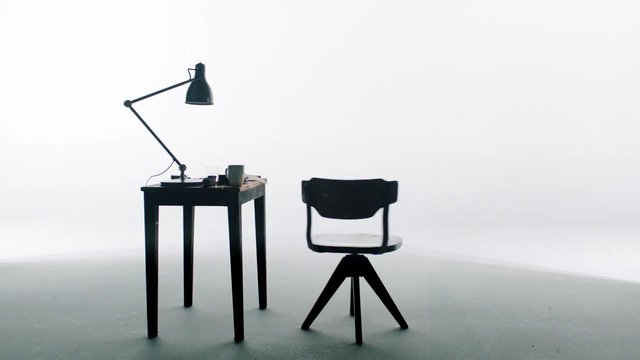 Video Reference: studio, minimalist, chair, table, desk lamp, black furniture, white background, interior, still life, simple setup, modern, lighting, empty room, furniture