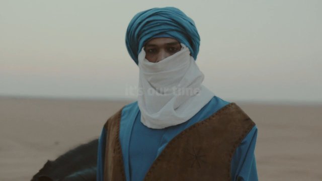 Video Reference: person, desert, traditional clothing, head wrap, face covering, outdoors, portrait, nomadic, sand, blue clothing, brown vest, landscape, human, travel, culture