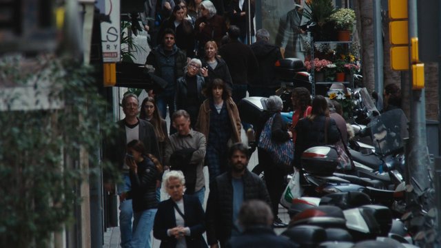 Video Reference: city street, pedestrians, crowd, urban, sidewalk, scooters, parked vehicles, storefronts, flowers, people walking, narrow street, downtown, outdoor, busy, street scene