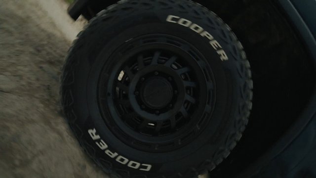 Video Reference: tire, wheel, rim, vehicle, off-road, close-up, black, dusty, sandy, ground, automotive, motion blur