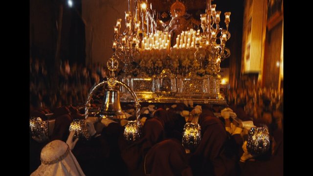 Video Reference: church, procession, candles, religious, float, crowd, robes, gold decoration, ornate, ceremony, indoor, festival, candlelight, altar, pilgrimage
