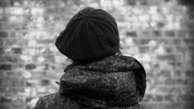 Video Reference: black and white, person, rear view, knit hat, coat, brick wall, blurred background, outdoor, winter clothing, portrait, back view, monochrome