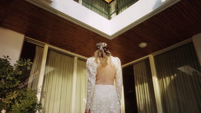 Video Reference: Wedding dress, Bridal clothing, Flash photography, Bridal party dress, Waist, Wood, Gown, Building, Plant, Fashion design