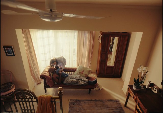 Video Reference: living room, family, parent and child, indoor, home interior, chaise lounge, window light, warm tones, domestic scene, bedroom decor, furniture, relaxing, aerial view, mother, father, child